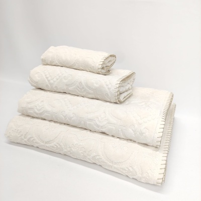 Conjunto de toalhas creme com padrão floral, empilhadas sobre fundo branco.