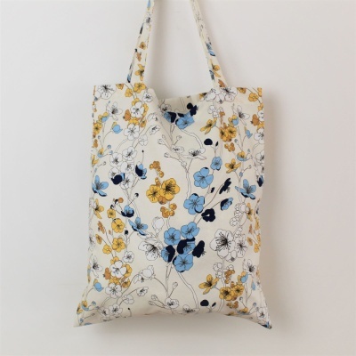 Saco de tecido branco com padrão floral azul, amarelo e preto