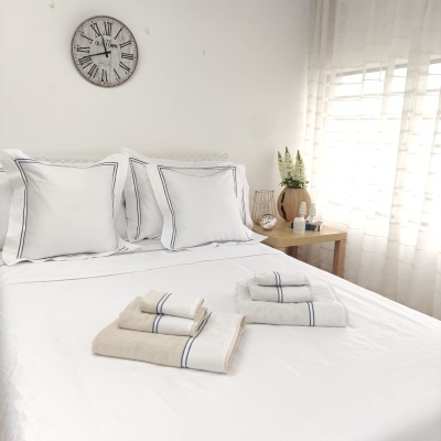 Cama com almofadas e lençóis brancos, toalhas dobradas, relógio de parede e móveis de madeira