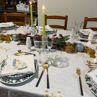 Mesa de jantar decorada para Natal com pratos florais, copos, talheres e velas acesas