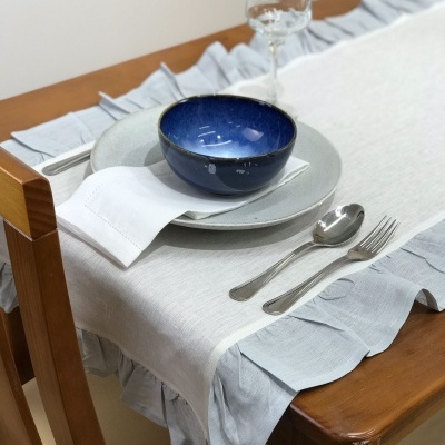 Mesa posta com louça, talheres e vidro sobre toalha com folhos