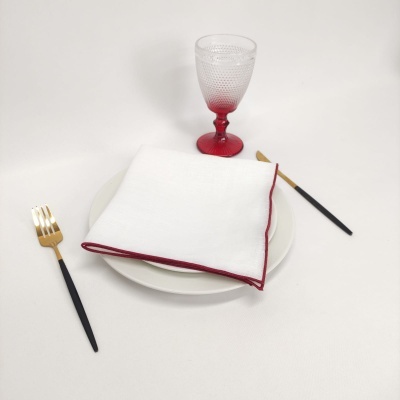 Prato branco com guardanapo branco e vermelhos, taça transparente com base vermelha e talheres preto e dourado