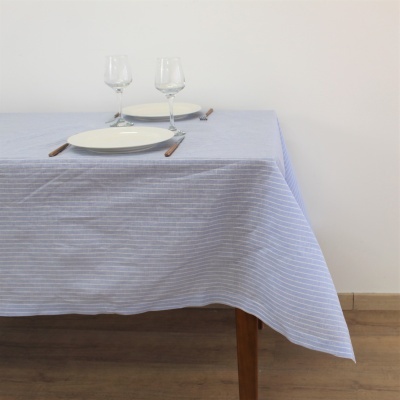 Toalha de mesa azul claro e branca listrada sobre mesa de madeira com pratos, copos e talheres