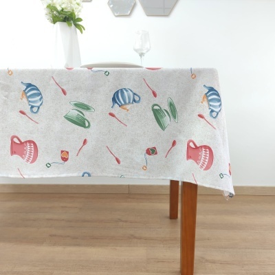 Toalha de mesa clara com padrão de bules coloridos e colheres, sobre mesa de madeira