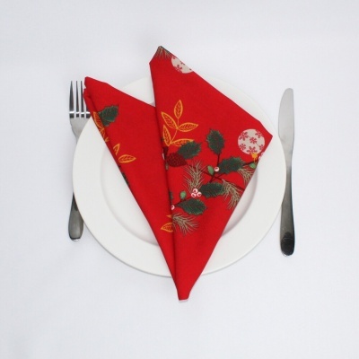 Guardanapo vermelho dobrado com padrões de folhas em prato branco com talheres