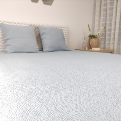 Cama com colcha azul claro e almofadas, cabeceira branca, mesa de cabeceira com vasos decorativos