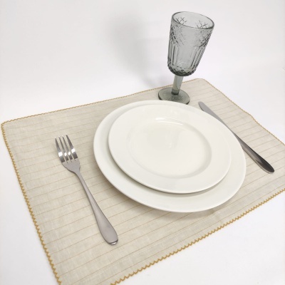 Conjunto de loiça branca, talheres metálicos e copo de vidro cinzento sobre individual bege decorativo