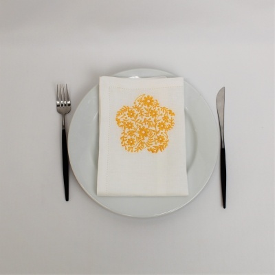 Guardanapo branco com estampa floral amarela sobre prato branco, com talheres pretos ao lado