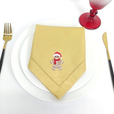 Guardanapo amarelo com bordado de boneco de gengibre no prato, talheres e copo vermelho
