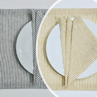 Porta-talheres de tecido às riscas em cinzento e bege sobre pratos brancos