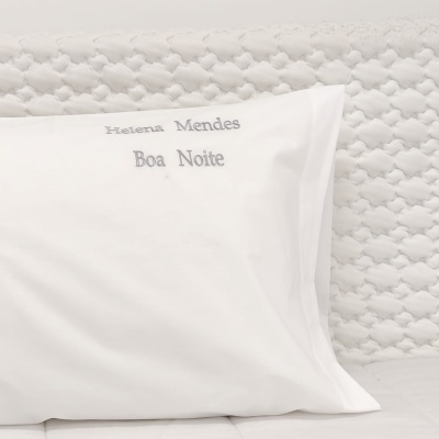 Travesseiro branco com fronha bordada e superfície texturizada branca ao fundo