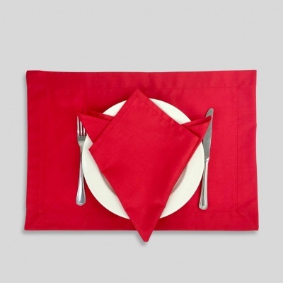 Conjunto guardanapo vermelho sobre prato branco com talheres em fundo cinzento