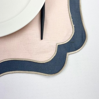 individuais de mesa em tecido rosa e azul com bordas bege, prato branco e talher preto sobre mesa branca