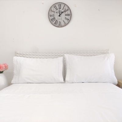 Cama com lençol e almofadas brancas bordadas e relógio de parede com números romanos