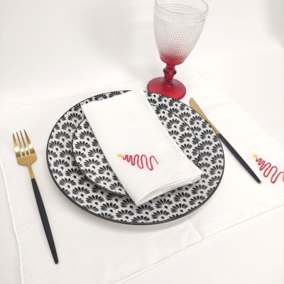 Conjunto de jantar com prato cerâmico padrão preto e branco, talheres preto e dourado, guardanapo branco bordado, copo rosa texturizado