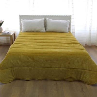 Cama com edredão mostarda acolchoado e almofadas brancas numa sala com mesa de madeira e cortinas brancas