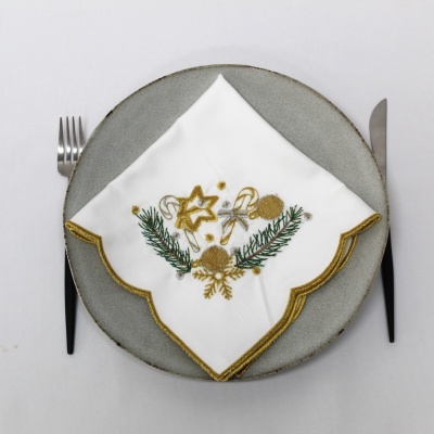 Guardanapo branco com bordado natalício em prato cinzento, talheres ao lado.