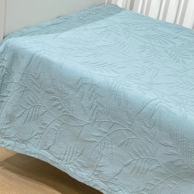 Colcha azul clara com padrão de folhas em cama branca