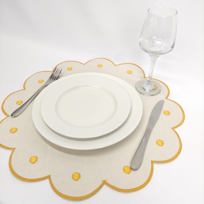 Conjunto de mesa com pratos brancos, talheres metálicos, copo de vidro e individual bege com bolinhas amarelas.