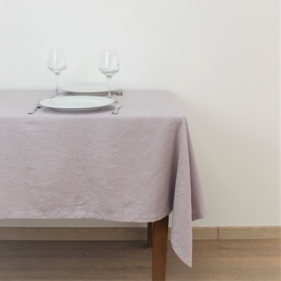 Mesa de madeira com toalha rosa clara, pratos brancos, talheres e copos de vidro para vinho