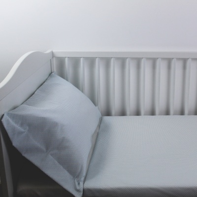 Berço branco com colchão e almofada cinza claro com padrão de pontos
