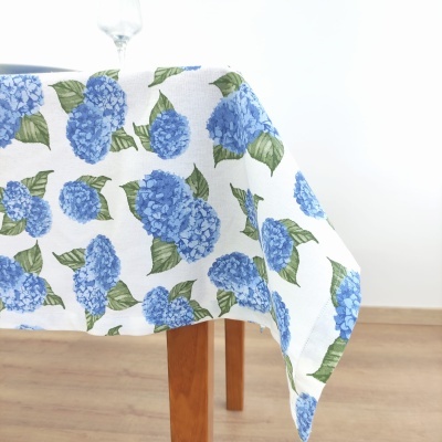 Toalha de mesa branca com flores azuis e folhas verdes sobre mesa de madeira