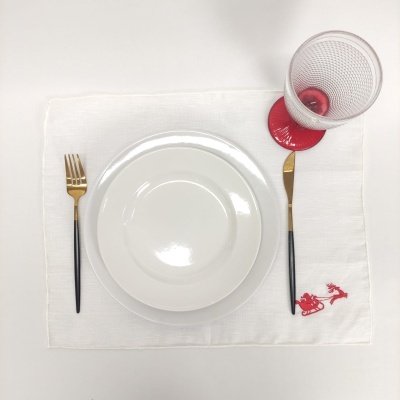 conjunto mesa com prato branco, talheres pretos e dourados, copo com base vermelha e jogo americano branco bordado