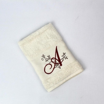 Toalha bege clara com bordado de letra 'A' bordô e detalhes florais castanhos