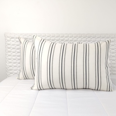Almofadas listradas pretas e brancas sobre cama branca com cabeceira trançada clara