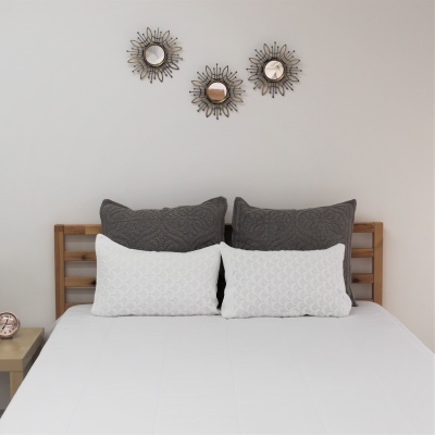 Cama com almofadas cinzentas e brancas, estrutura de madeira, espelhos decorativos redondos na parede branca