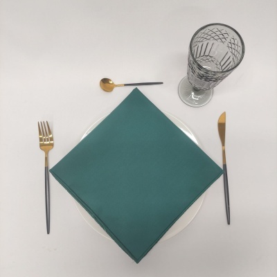 Conjunto de talheres e guardanapo em arranjo de mesa com copo de vidro.