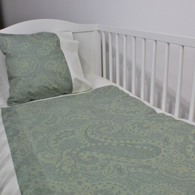 Cama de bebé branca com roupa de cama verde de padrão floral