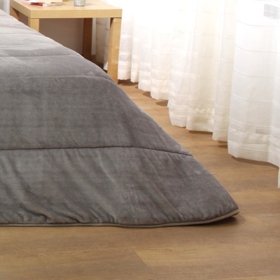 Colcha cinzenta macia em cama, com cortinas brancas e chão de madeira