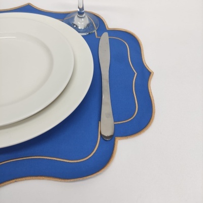 Mesa posta com pratos brancos, sousplat azul com bordas douradas e faca ao lado