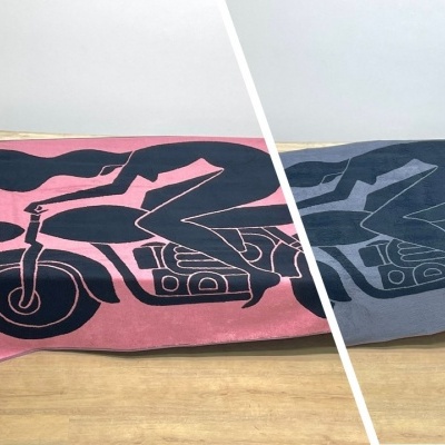 Tapetes retangulares rosa e cinza com estampa preta de motociclista sobre motocicleta em piso de madeira.