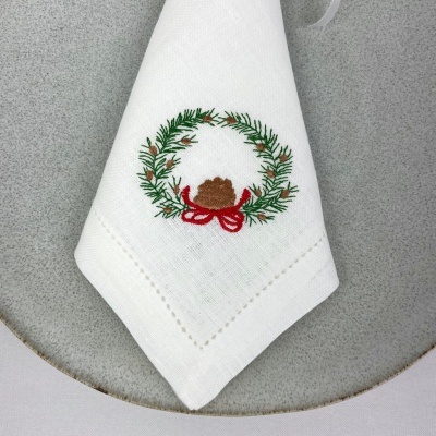 Guardanapo branco com bordado de grinalda e laço vermelho sobre prato cinza