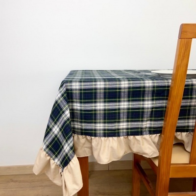 Toalha de mesa xadrez azul, branco e verde com barra bege numa mesa de madeira clara com cadeira ao lado