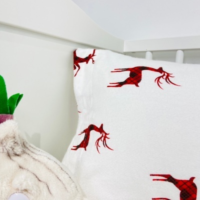 Travesseiro branco com padrão de rena vermelha em cama branca