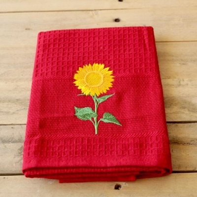 Toalha de cozinha vermelha com bordado de girassol sobre mesa de madeira