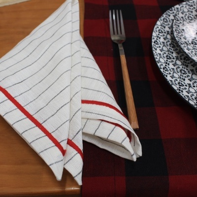 guardanapo branco com riscas pretas e bordas vermelhas ao lado de prato e tigela brancos com padrões florais pretos e pano vermelho e preto xadrez