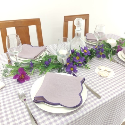 Mesa de jantar com toalha xadrez lilás, pratos brancos, guardanapos lilás, copos e flores artificiais roxas