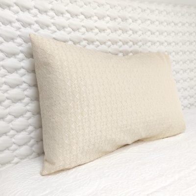 Almofada bege claro com padrão texturizado sobre cama branca com colcha de padrão de nó.