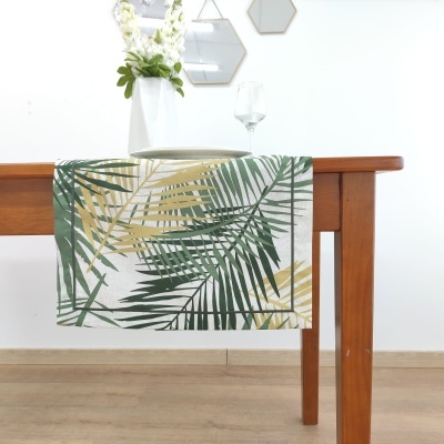 Toalha de mesa com padrão de folhas verdes e amarelas pendurada numa mesa de madeira