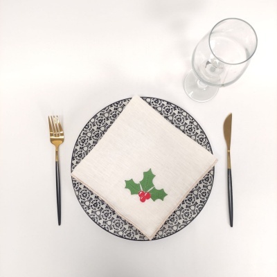 Mesa posta com prato decorado, guardanapo bordado, talheres e taça de vidro.