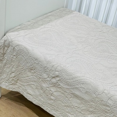 Colcha bege claro com padrão texturizado sobre cama branca