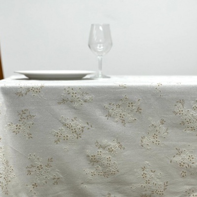Toalha de mesa branca com padrão floral, cadeira de madeira, prato branco e taça de vidro