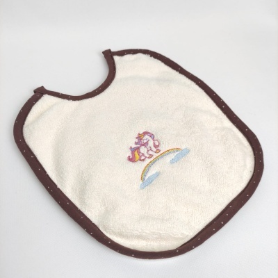 Babete de bebé branco com bordas castanhas e bordado de unicórnio e arco-íris