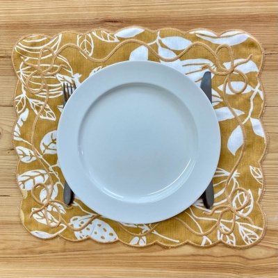 Prato branco sobre individual amarelo com padrão de folhas e talheres em mesa de madeira