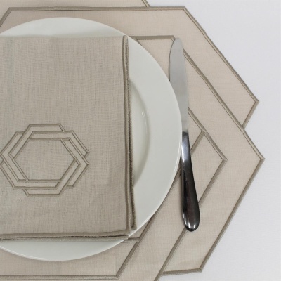 Conjunto de mesa com prato branco, guardanapo bege bordado, faca prateada e base hexagonal de tecido bege