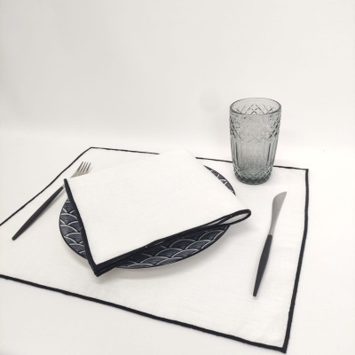 Conjunto de mesa com placemat branco, prato azul, guardanapo branco, copo cinzento e talheres pretos